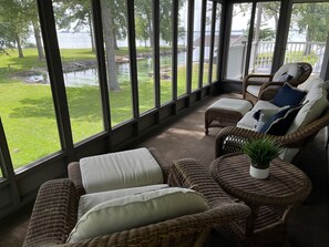 Une véranda meublée de mobilier en osier, dotée de grandes fenêtres et offrant une vue sur un lac.