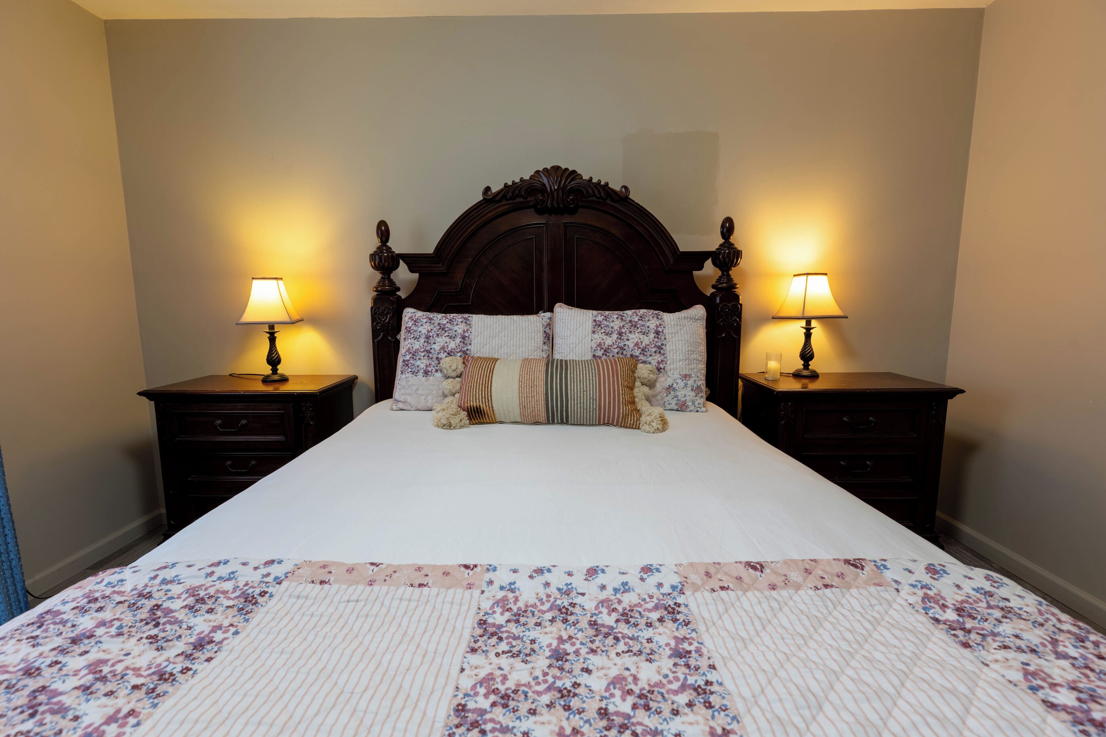 A bed with a floral quilt, two bedside lamps, and a dark wooden headboard.
