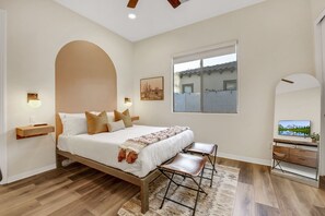 Une chambre à coucher avec un lit, des tables de chevet, un bureau et une grande fenêtre.