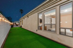 Un couloir d’hôtel avec un revêtement de sol vert en gazon synthétique, de grandes fenêtres et un ciel étoilé.
