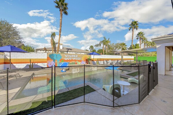 An outdoor pool area with a glass enclosure, palm trees, and a mural on the wall.
