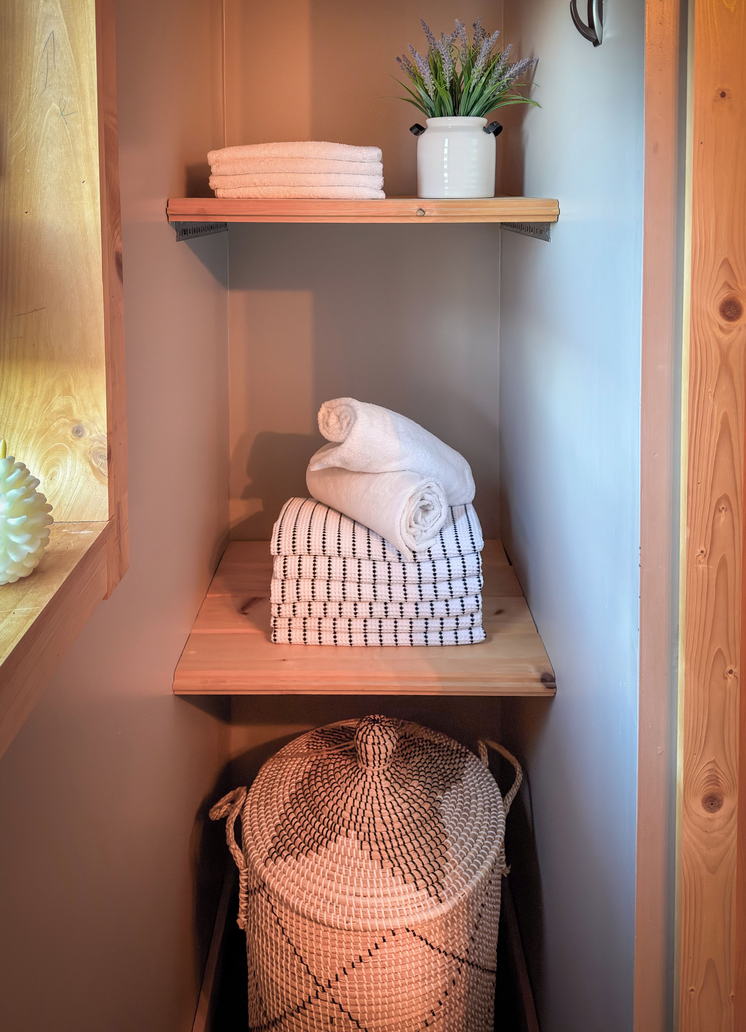 Une salle de bain avec des étagères en bois où sont rangées des serviettes et une plante en pot.