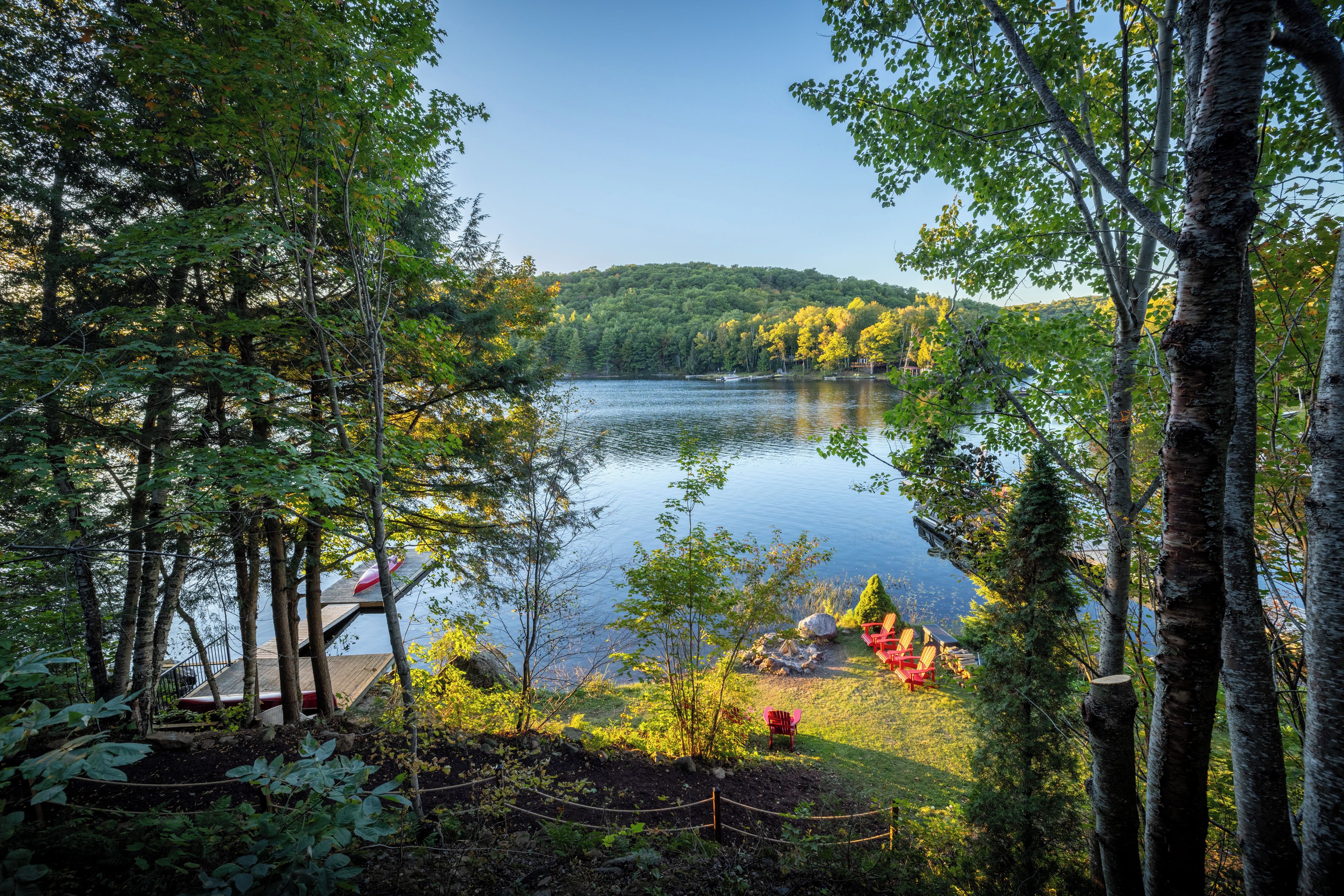 A lakeside view with a dock, chairs, and a small cabin.