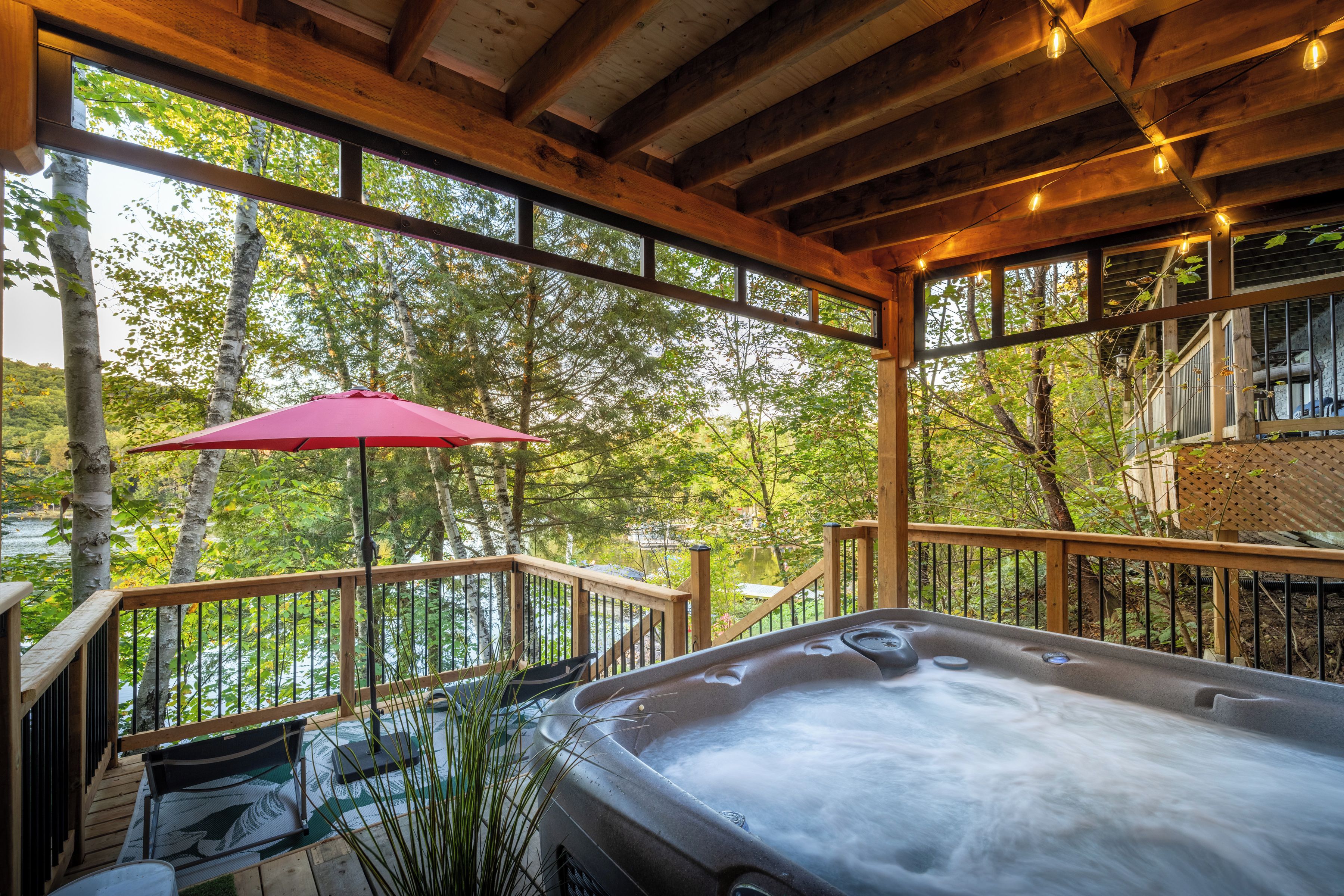 A hot tub in a wooden deck area with a view of trees and a red umbrella.