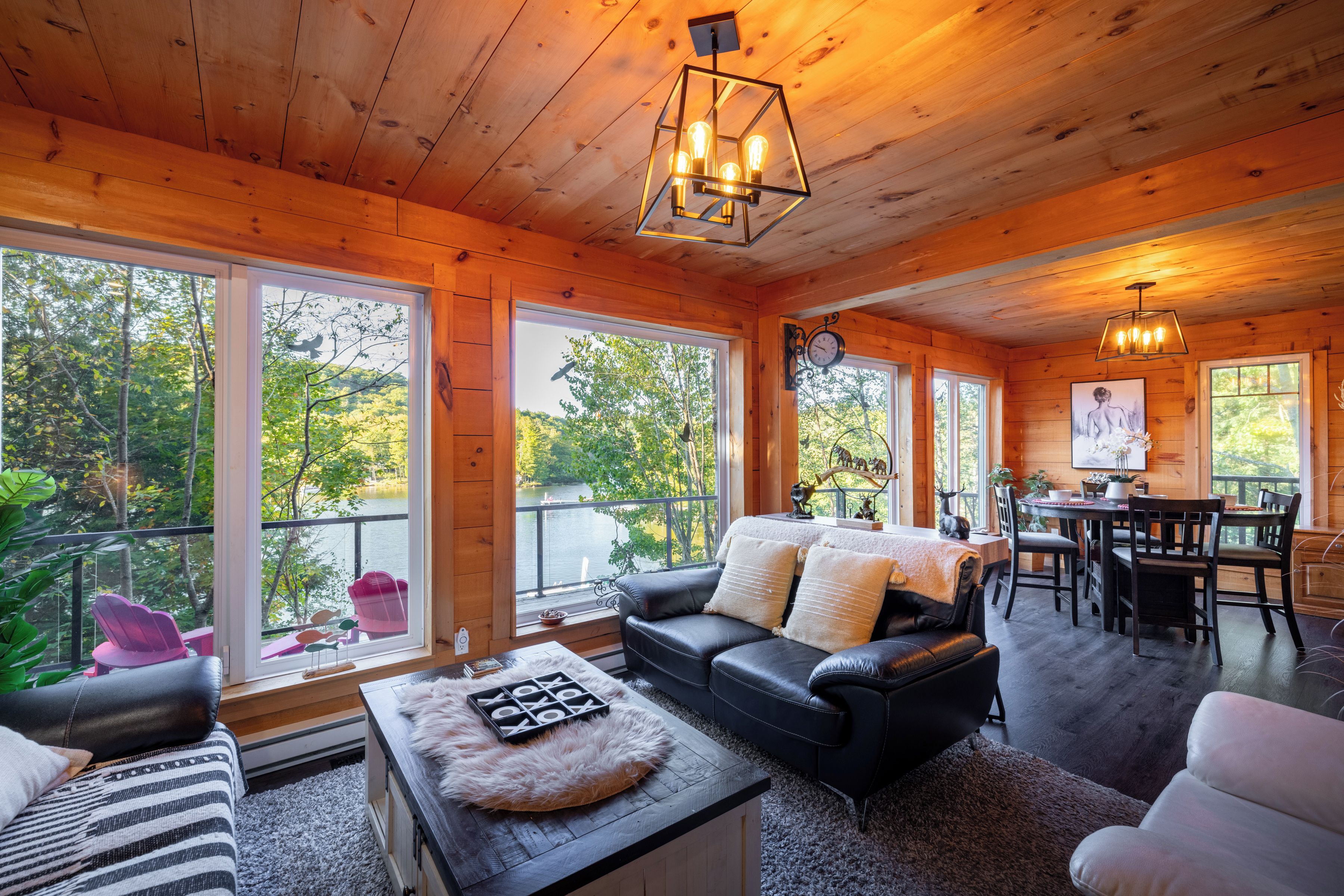 Ein gemütliches Blockhaus-Interieur mit Essbereich, Kamin und großen Fenstern mit Blick auf einen Wald.