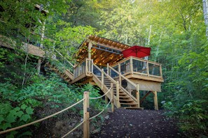 A wooden deck with a red umbrella, surrounded by dense forest. - Eagle's Nest on Raven Lake | Panoramic View | Hot Tub & Sauna | Lakefront Escape (Dorset)