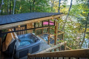 A hot tub on a wooden deck with a view of a forest. - Eagle's Nest on Raven Lake | Panoramic View | Hot Tub & Sauna | Lakefront Escape (Dorset)