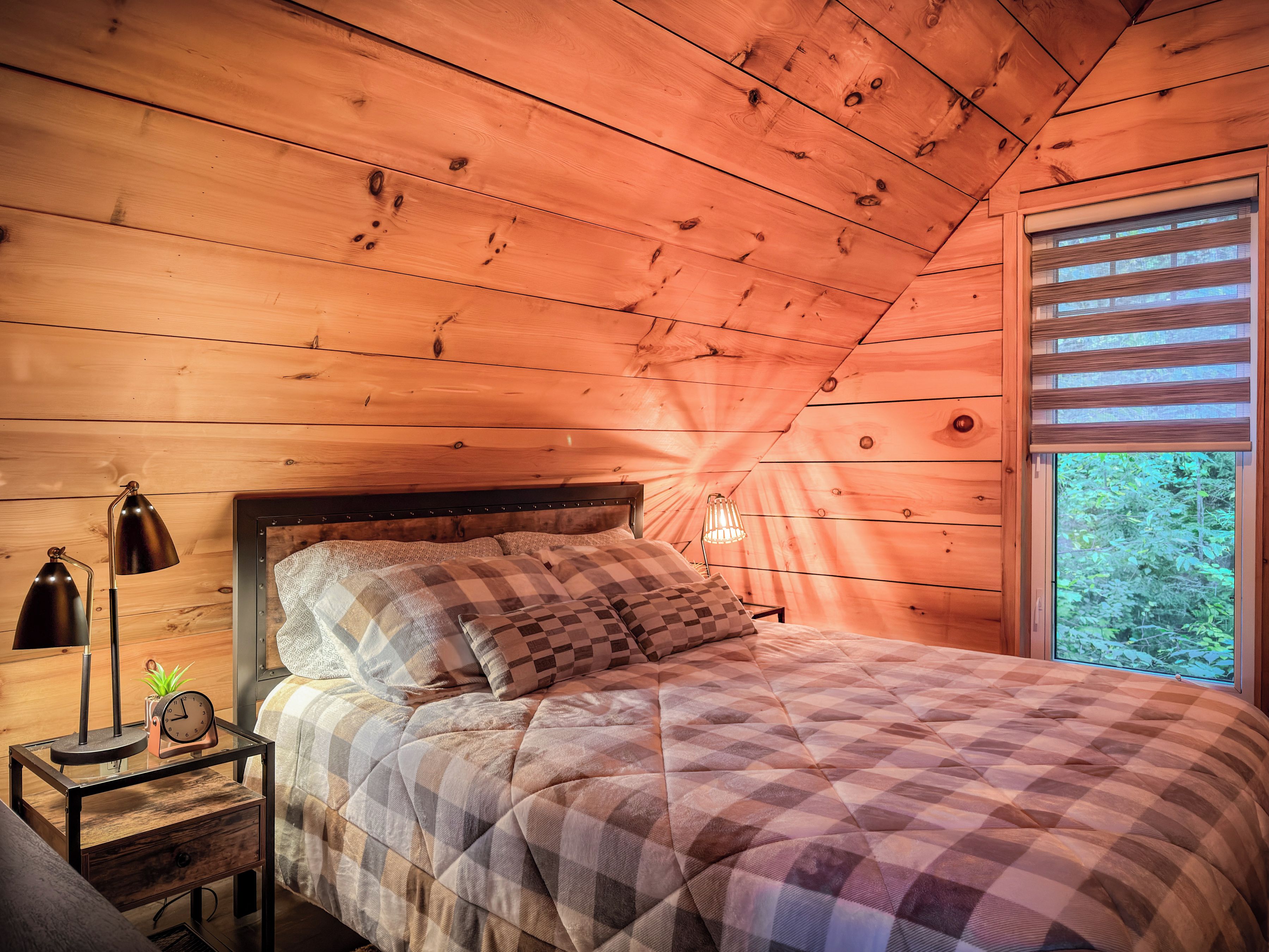 A wooden cabin bedroom with a bed, a nightstand, a lamp, and a window.