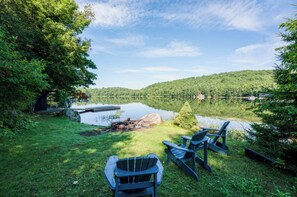 Un espace extérieur aménagé au bord du lac, avec des chaises Adirondack, un petit foyer et une jetée qui s’avance sur l’eau.