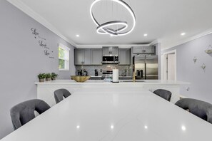 A modern kitchen with grey cabinets, a white island, and a central island with a bowl. There are potted plants on the counter and a wall decal with the words "Live Laugh Love." - Charlotte Spacious Home (Charlotte)