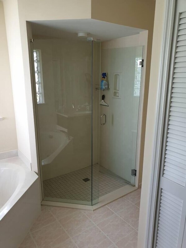A glass-enclosed shower with a tiled floor, a white bathtub, and a door with a handle.