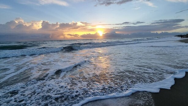 Une plage avec des vagues et un coucher de soleil.