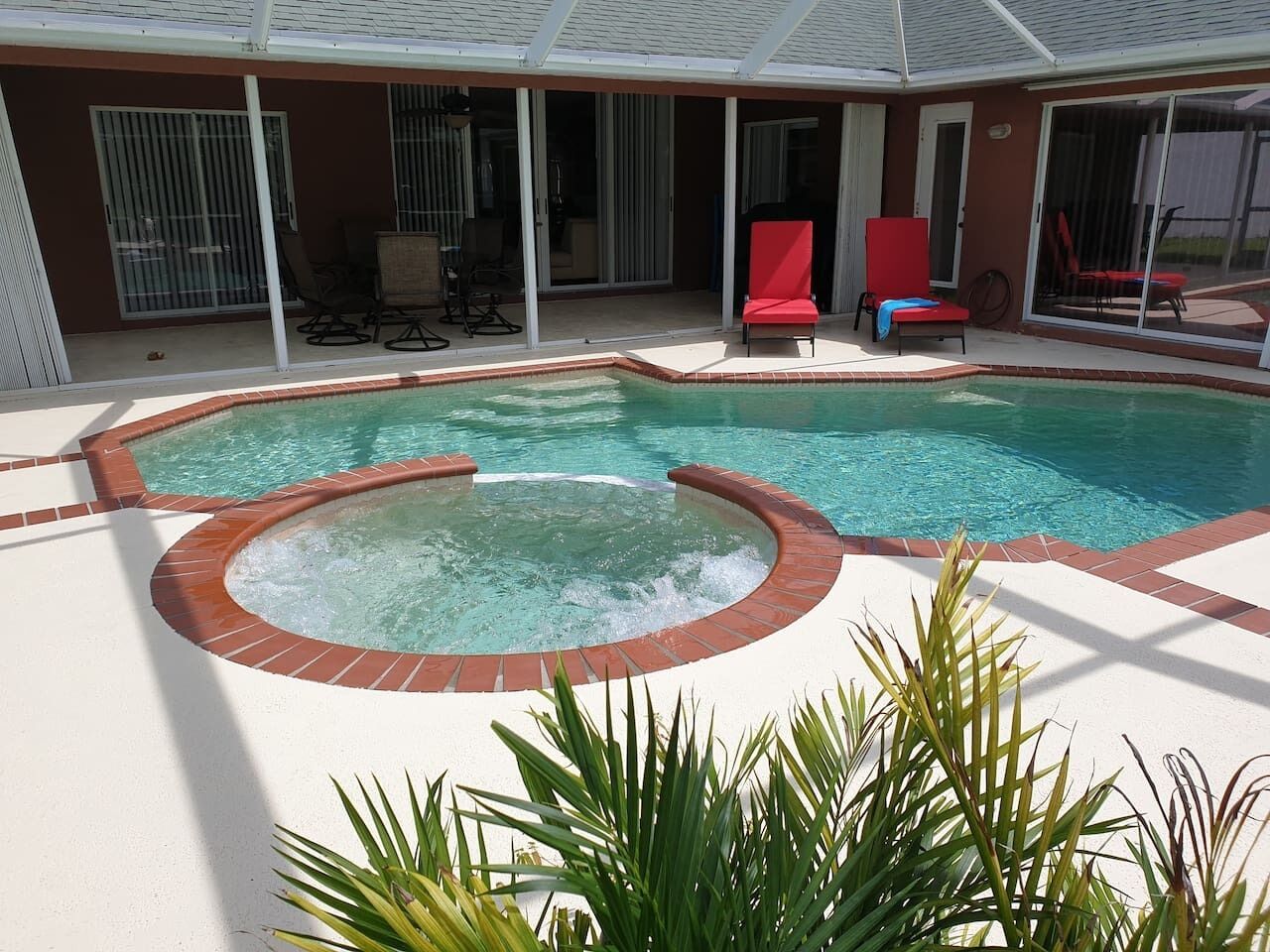 A pool area with a hot tub, lounge chairs, and a covered patio.