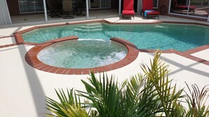 Un espace piscine comprenant un jacuzzi, des chaises longues et un patio couvert.