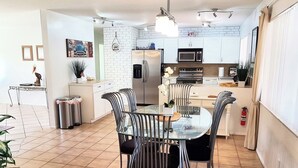Une cuisine moderne avec des meubles blancs, un réfrigérateur en acier inoxydable et un four à micro-ondes. On y trouve une table à manger avec quatre chaises et un plateau en verre.