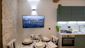 A dining area with a TV mounted on the wall displaying a scenic view, a kitchen with green cabinets, and a dining table set with plates, glasses, and cutlery.