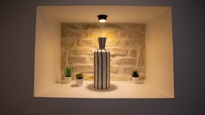 A modern interior with a textured stone wall, a central cylindrical vase, and small potted plants on a white shelf.