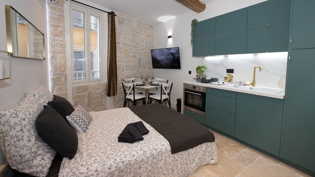 A bedroom with a bed, a desk, and a kitchenette.
