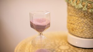 An hourglass with pink sand on a round table.
