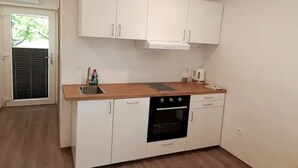 Une cuisine avec des meubles blancs, un plan de travail en bois, un four encastré et une fenêtre avec des stores.
