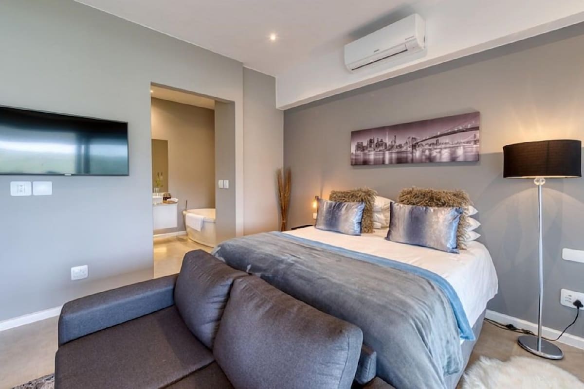 A modern bedroom with a bed, a flat-screen TV, a floor lamp, and a painting on the wall.