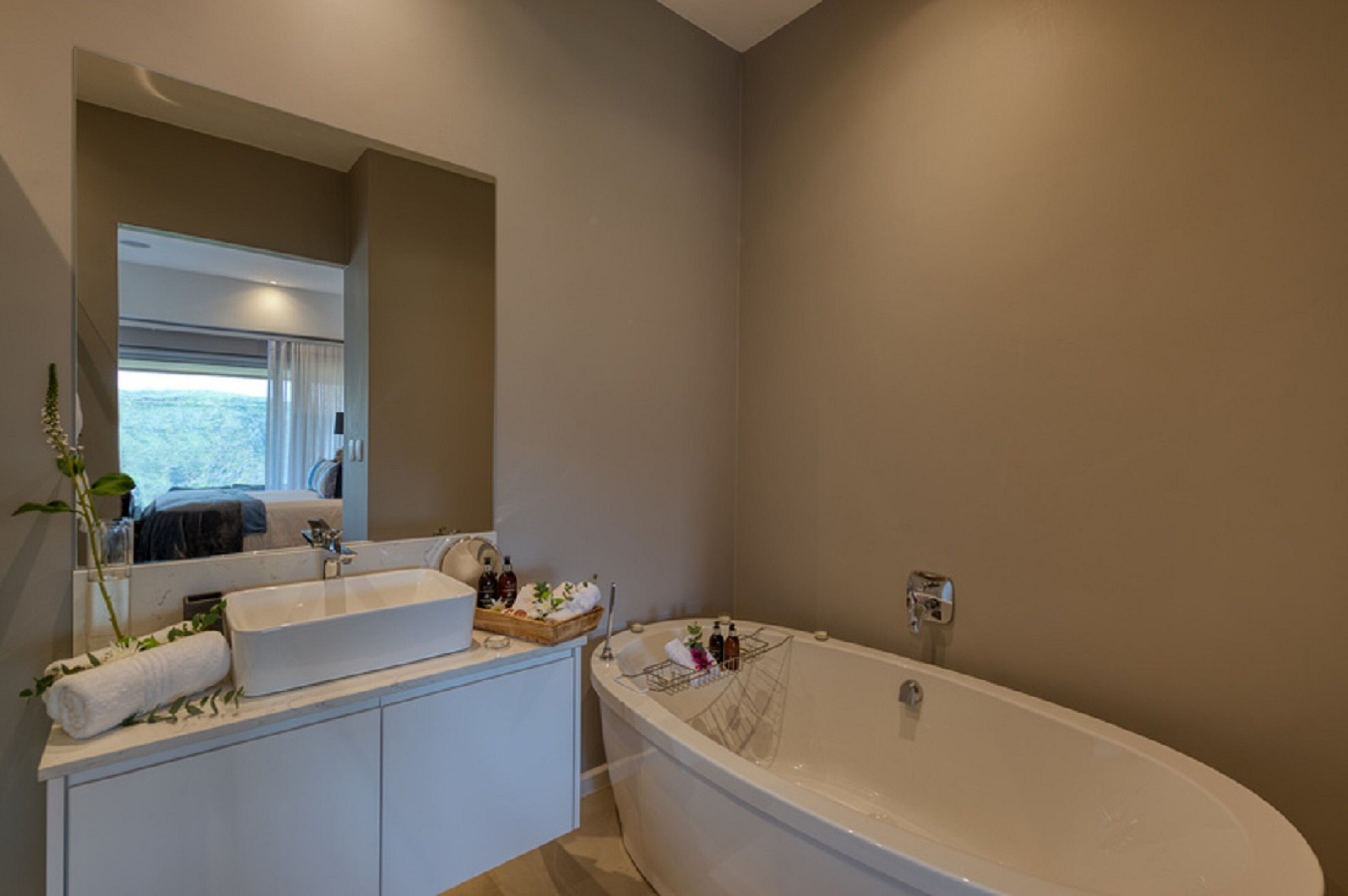 Een moderne badkamer met een vrijstaand bad, een wastafel met spiegel en een raam dat uitzicht biedt op de omgeving.