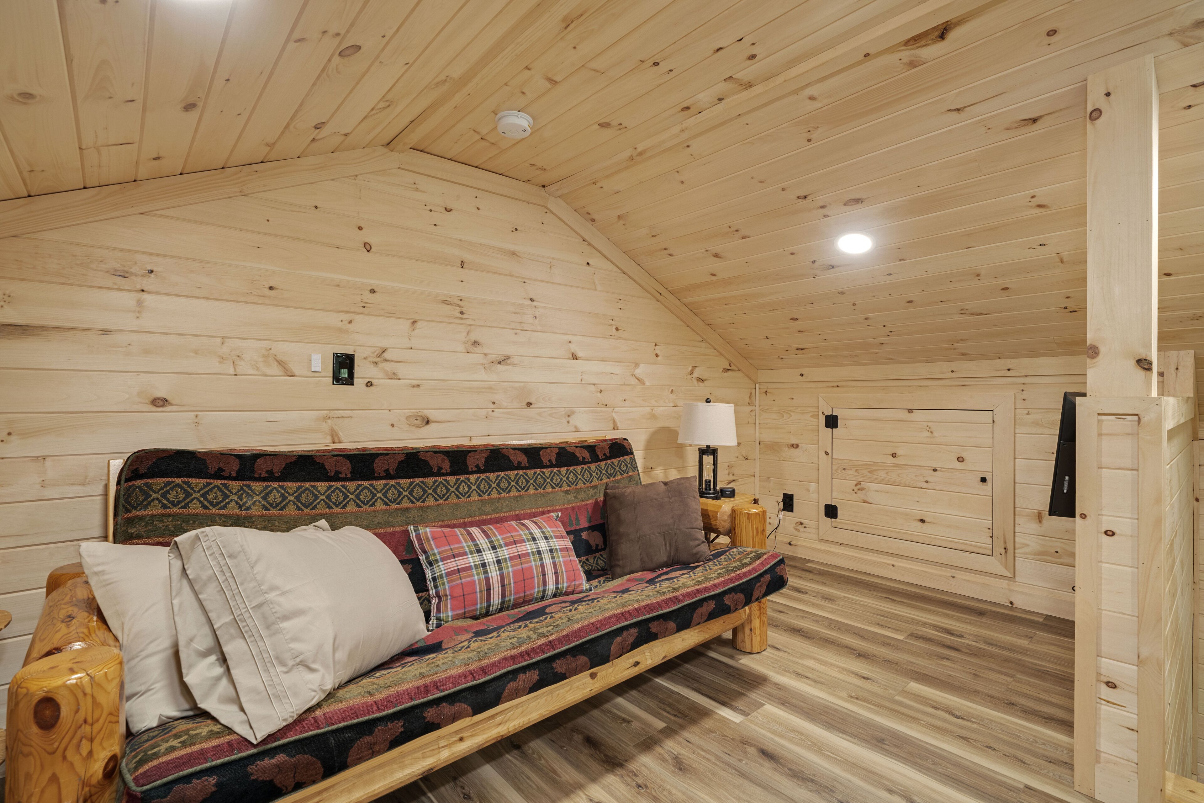 Interior acogedor de una cabaña de madera con un sofá, almohadas, una lámpara y una luz en el techo.