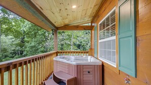 Een houten terras met een hottub, een zitje en uitzicht op het omliggende bos.