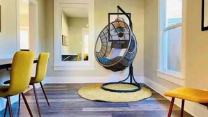 A dining area with a round table, yellow chairs, a hanging egg chair, and a view of the adjacent room through a doorway.