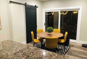 Un coin repas avec une table ronde, des chaises jaunes, une plante en pot et une porte coulissante.