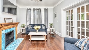 A living room with a fireplace, a ceiling fan, a sofa, a coffee table, and a door with glass panels.