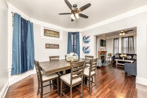 A dining area with a wooden table and chairs, a ceiling fan, and a fireplace in the background.