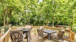 A wooden deck with a table and chairs, surrounded by a wooden railing and trees.