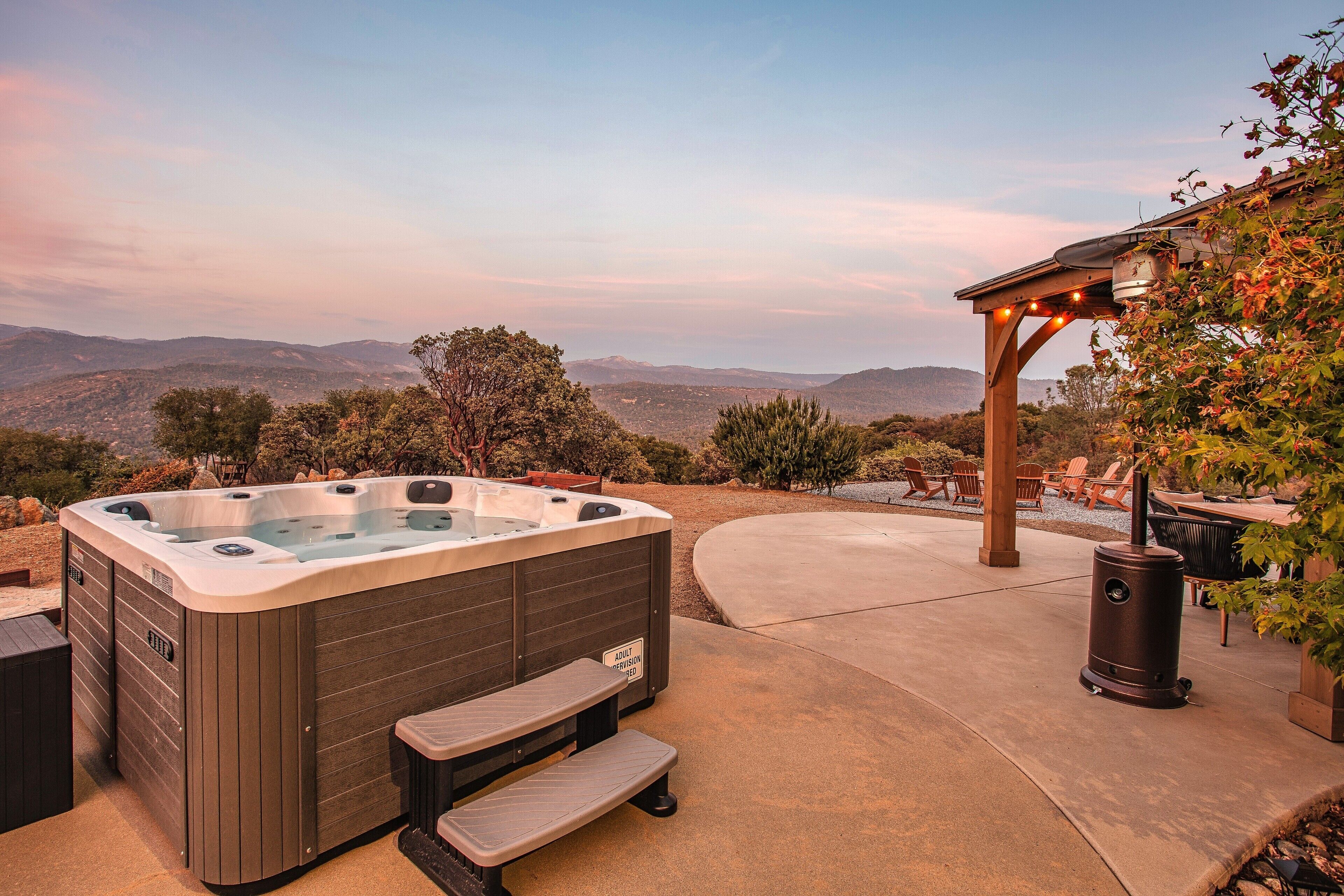A hot tub with a view of mountains, a pergola, and outdoor seating.