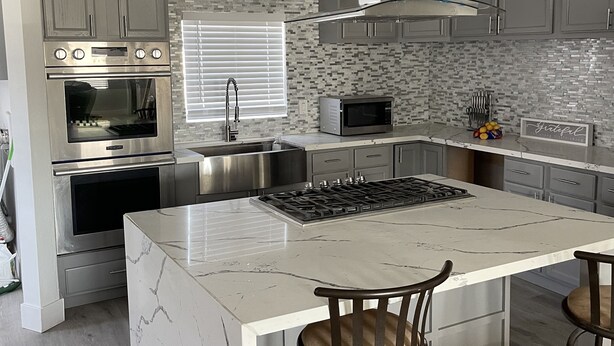 A modern kitchen with a central island, stainless steel appliances, and grey cabinetry. - Cozy ranch house with indoor pool (Norco)