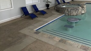 A pool area with a stone hot tub, blue lounge chairs, and a flat-screen TV mounted on the wall. - Cozy ranch house with indoor pool (Norco)