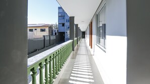 A corridor with a green balustrade, a tiled floor, and a view of buildings in the background. - Vila Nóbrega Residencial (Foz do Iguaçu)