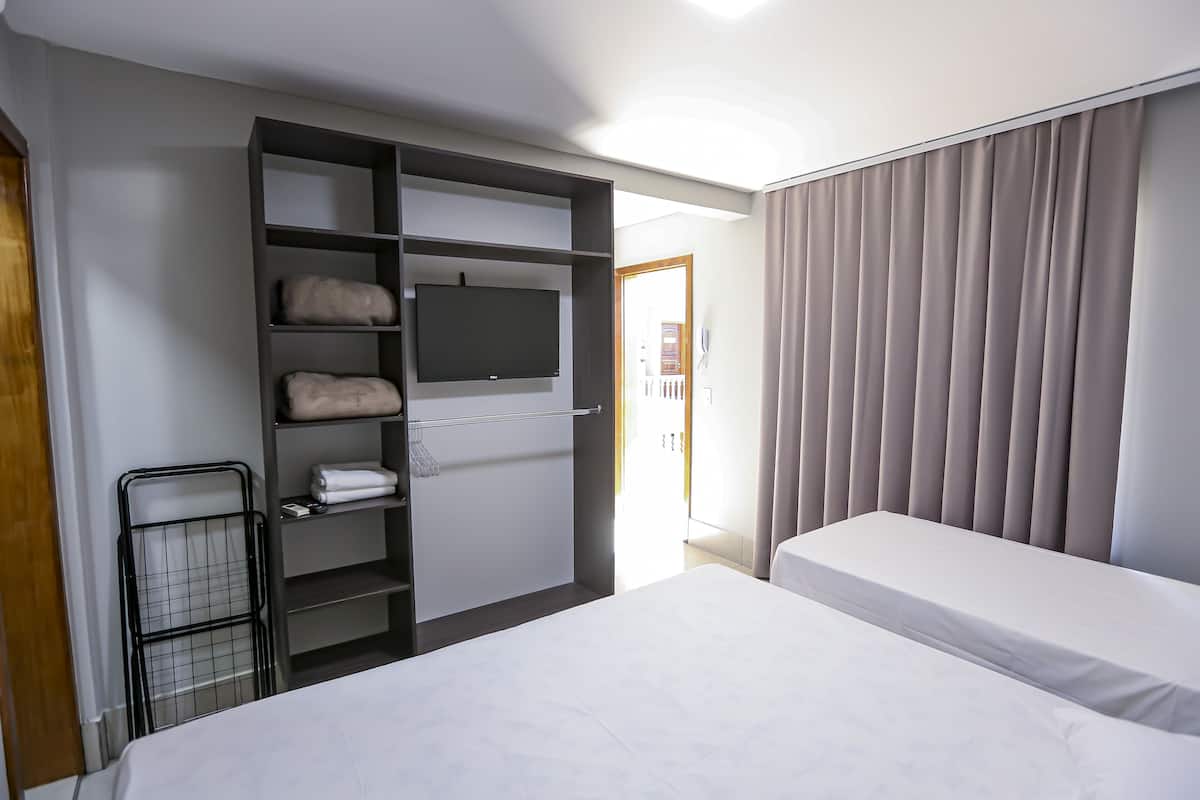 A hotel room with a bed, a TV mounted on a wall, a wardrobe, and a window with curtains.