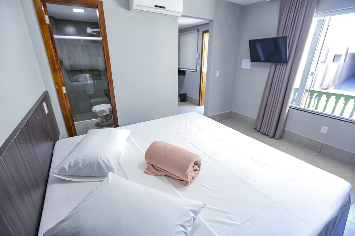 A hotel room with a bed, a TV mounted on the wall, and a window with curtains.