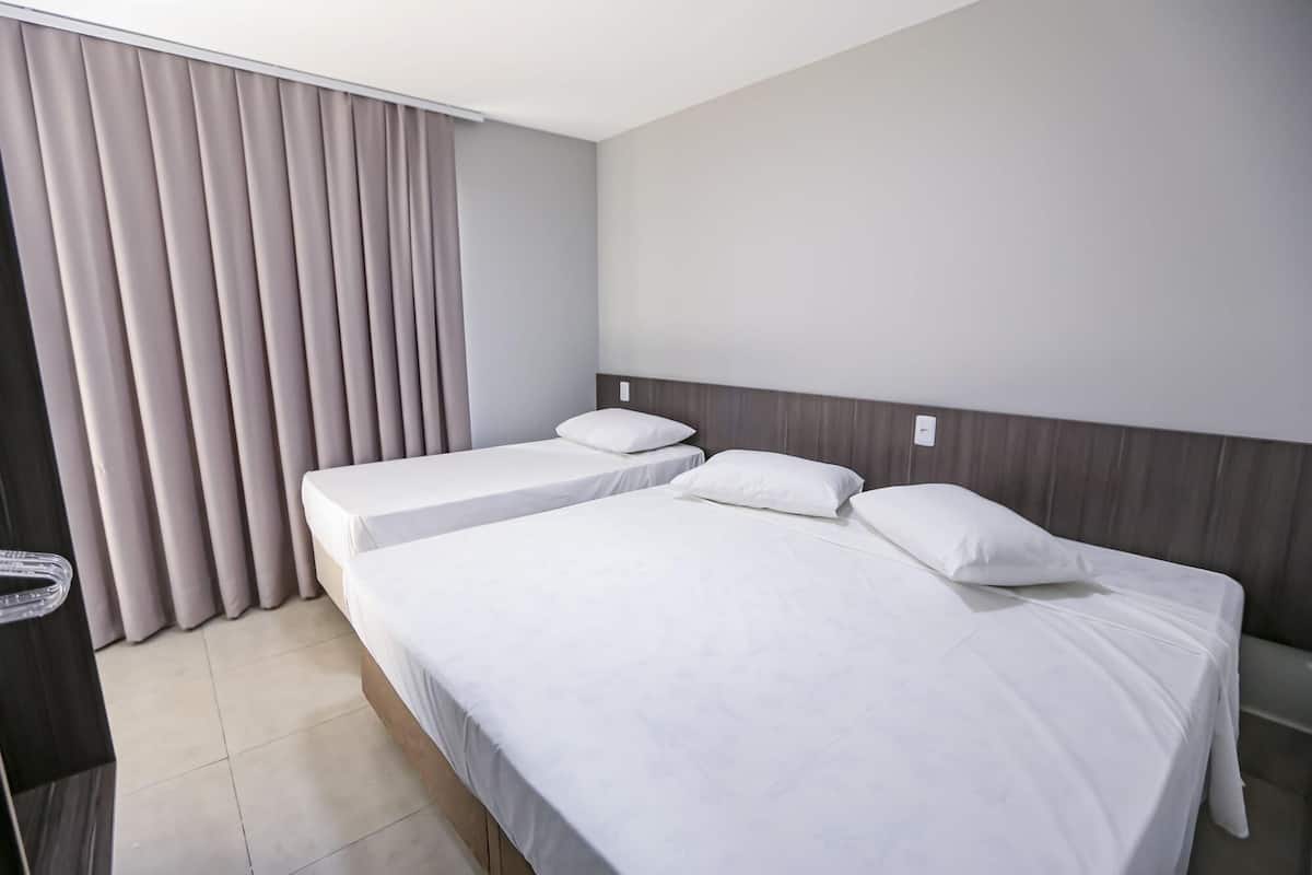 A hotel room with two beds, a large window with curtains, and a tiled floor.