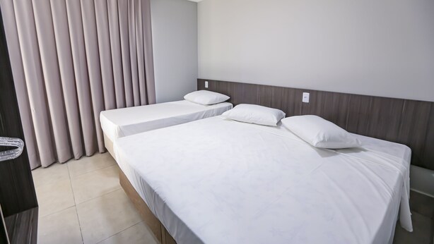 A hotel room with two single beds, a wooden headboard, a large window with curtains, and a tiled floor. - Vila Nóbrega Residencial (Foz do Iguaçu)