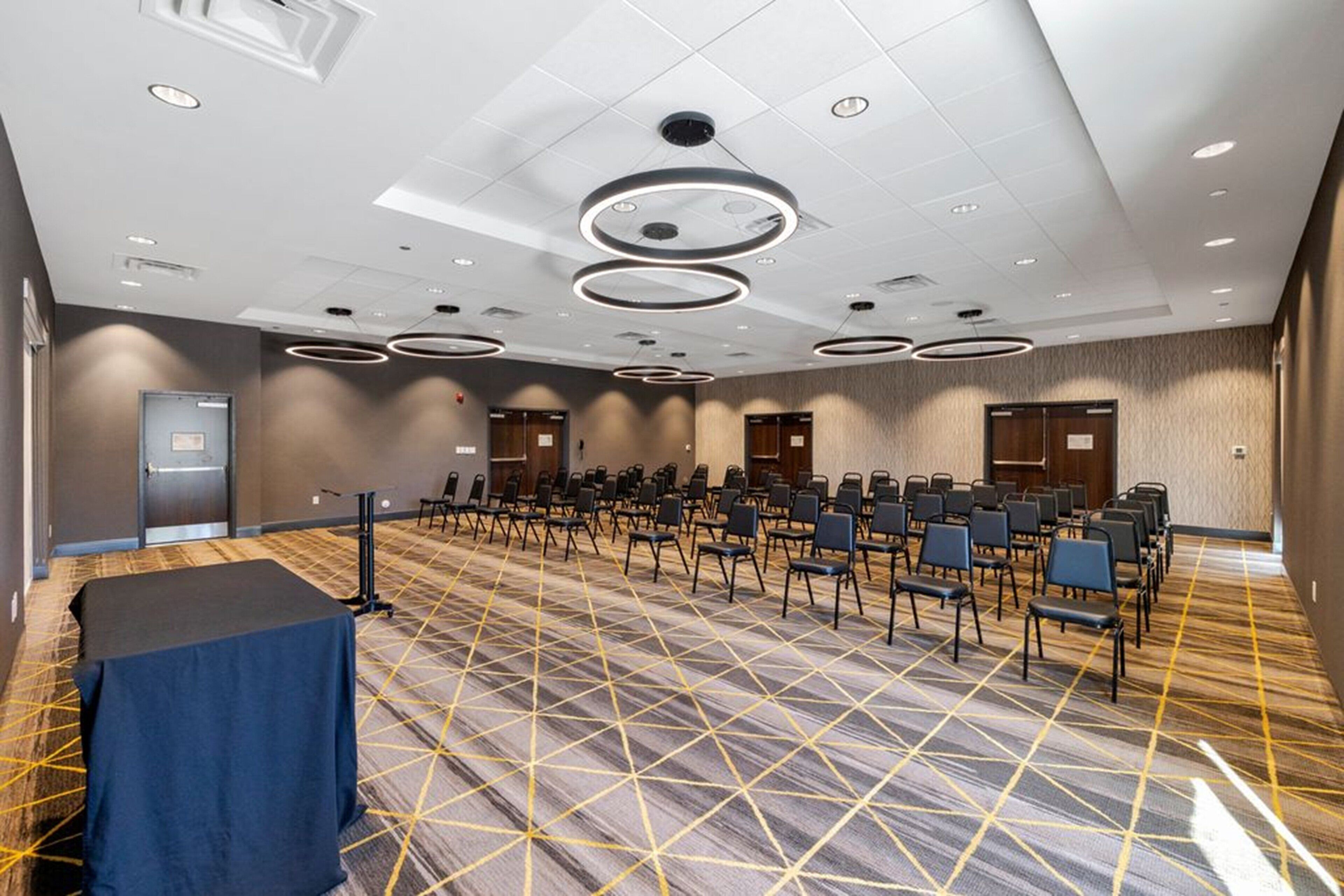 A conference room with rows of chairs, a table, and a patterned carpet.