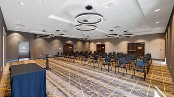 A conference room with rows of chairs, a table, and a patterned carpet.