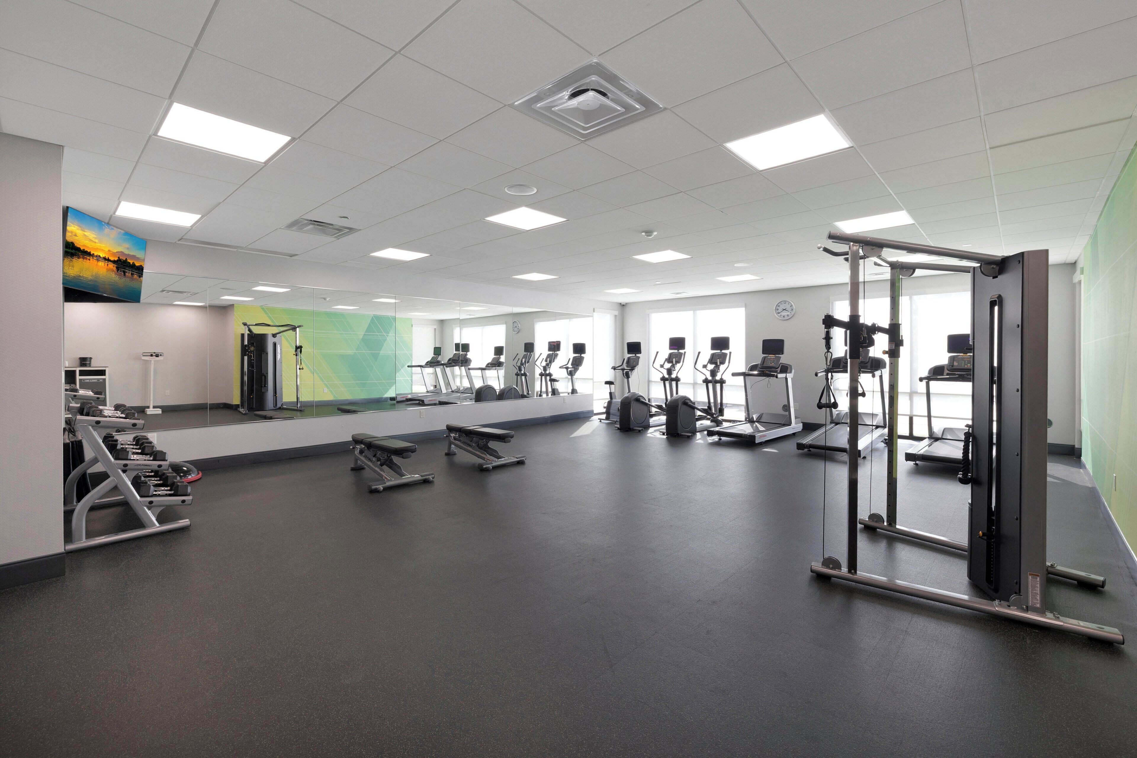 A spacious gym with various exercise equipment, large windows, and a green wall.