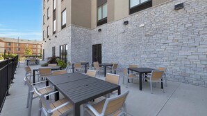 An outdoor patio area with tables and chairs, a stone wall, and a building in the background.
