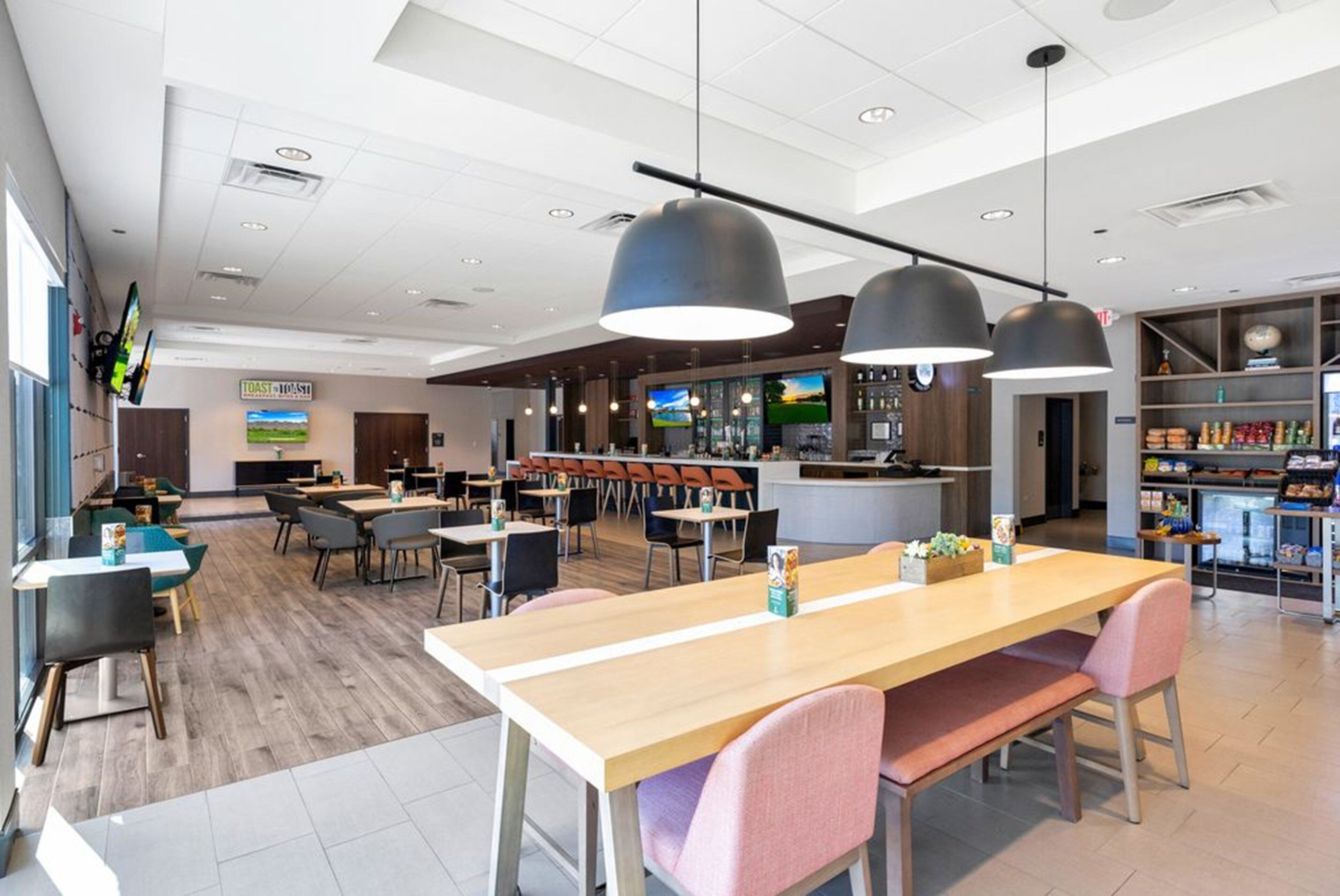 A modern restaurant with wooden tables and chairs, a bar area, and a TV screen displaying a scenic view.