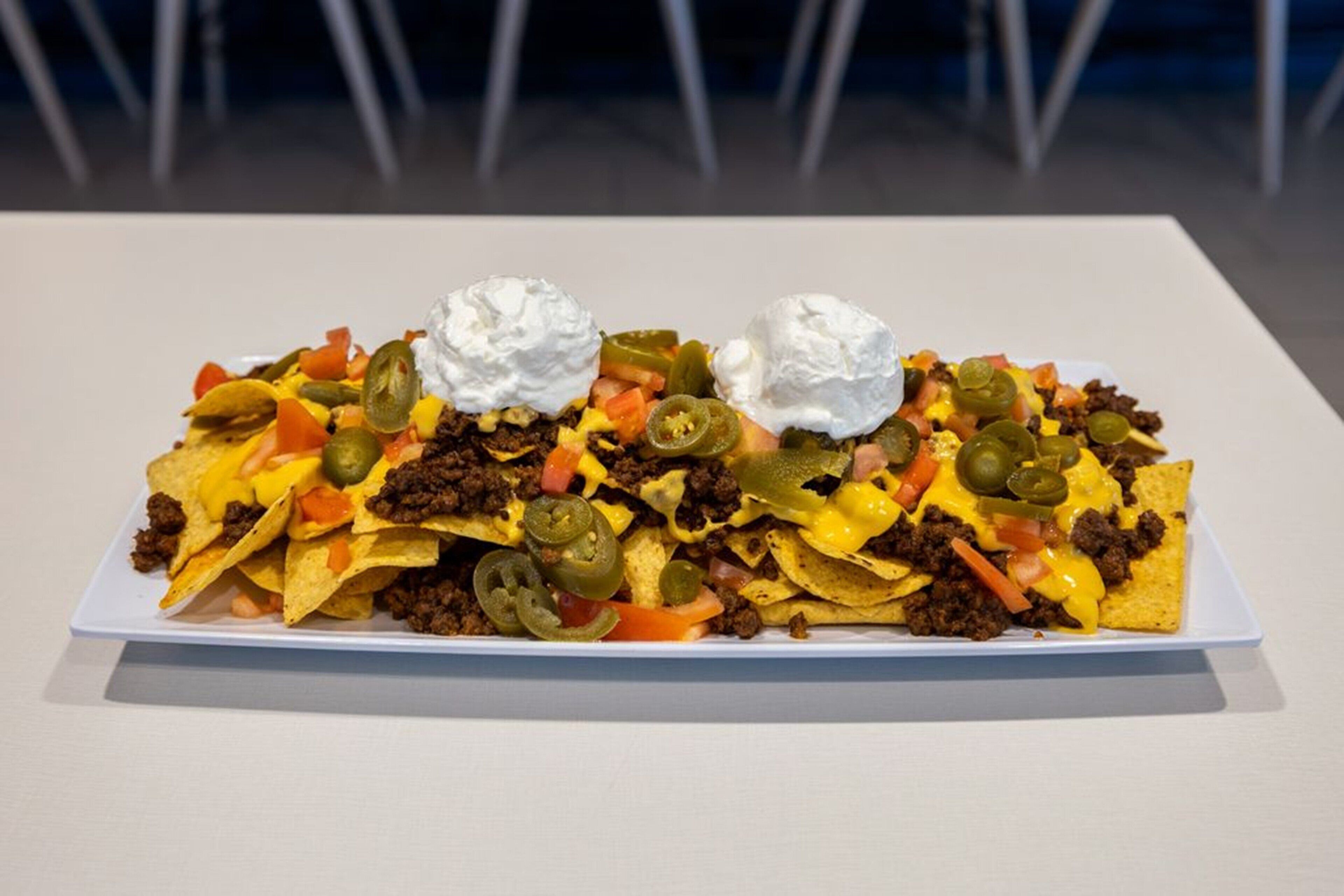 A large plate of nachos with toppings and whipped cream on a white table.