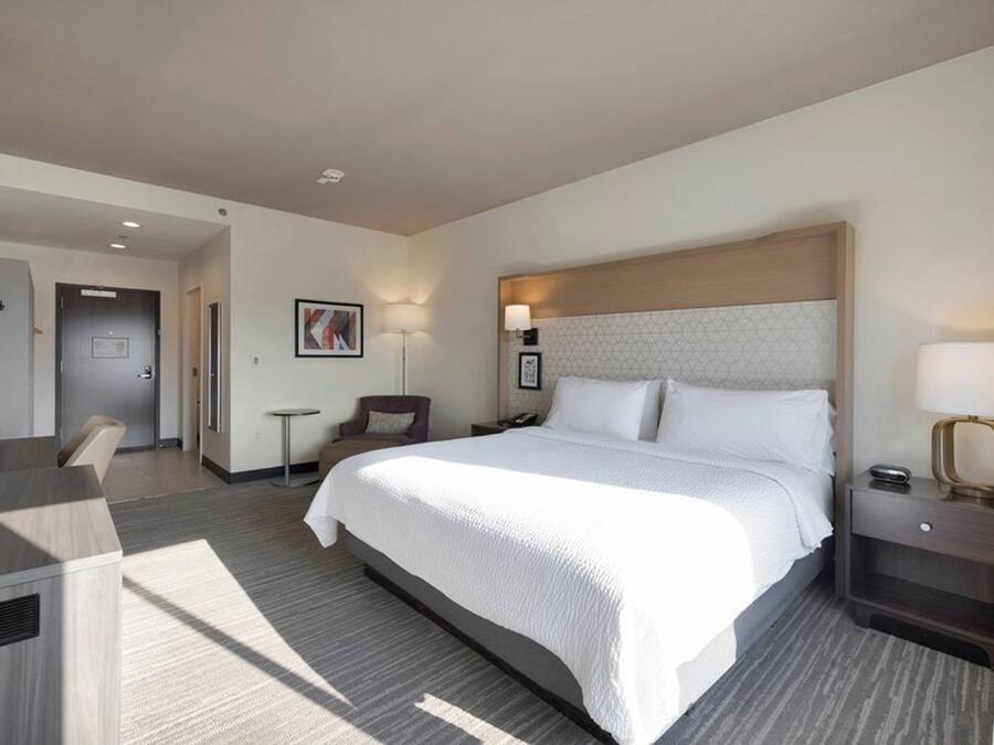 A modern hotel room with a large bed, a desk, a chair, and a TV.