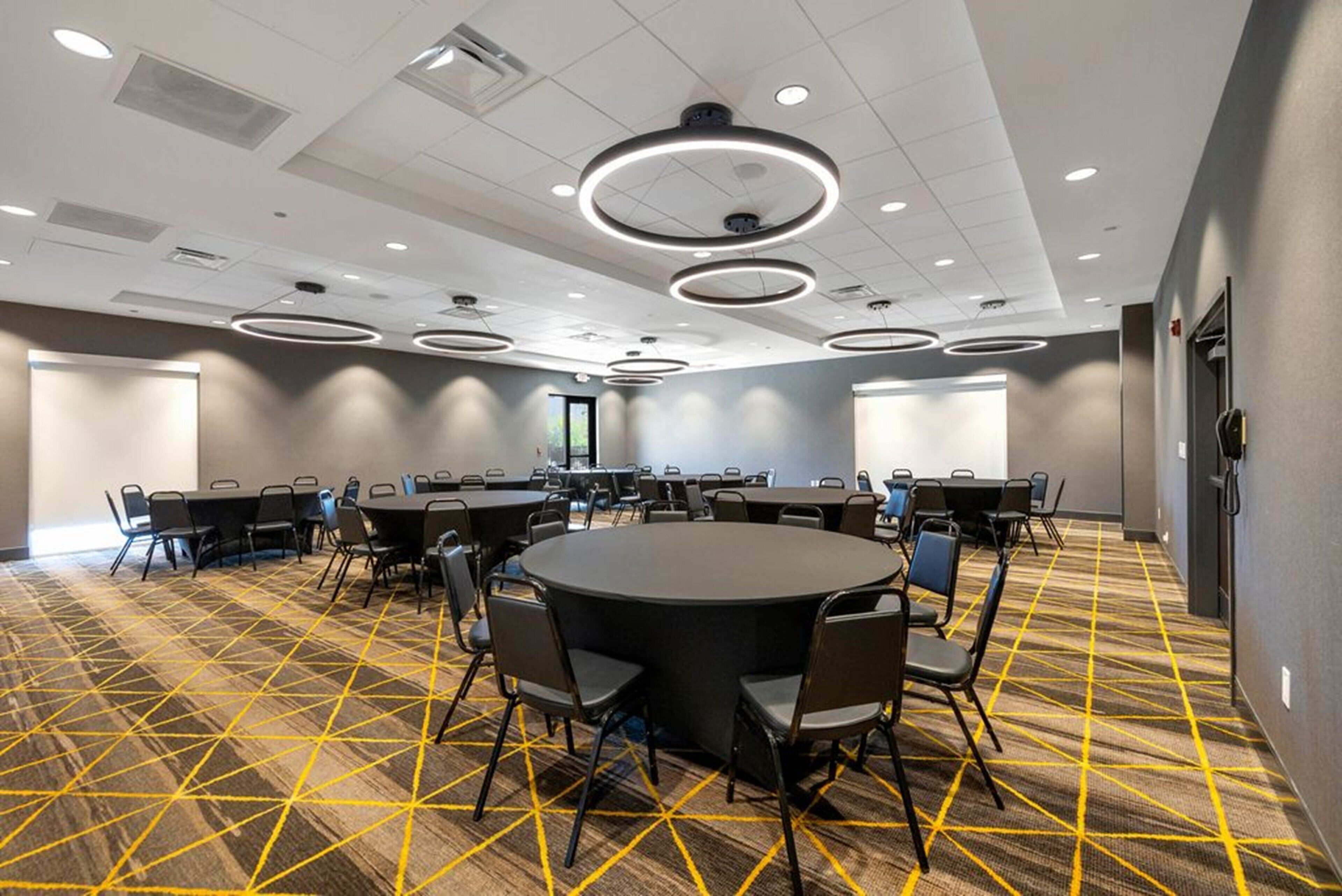 A conference room with a large round table surrounded by chairs, a patterned carpet, and circular ceiling lights.