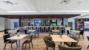 A modern cafe with multiple seating areas, a bar, and a display of beverages.